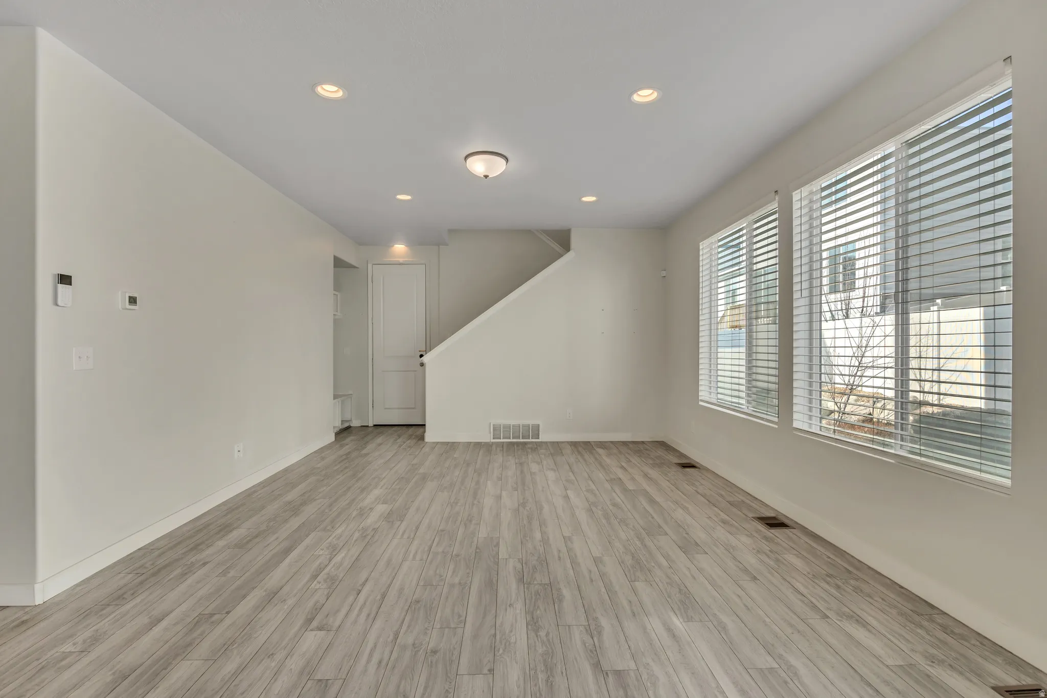 Spacious room featuring wood-finish flooring, recessed lighting, and multiple windows with blinds