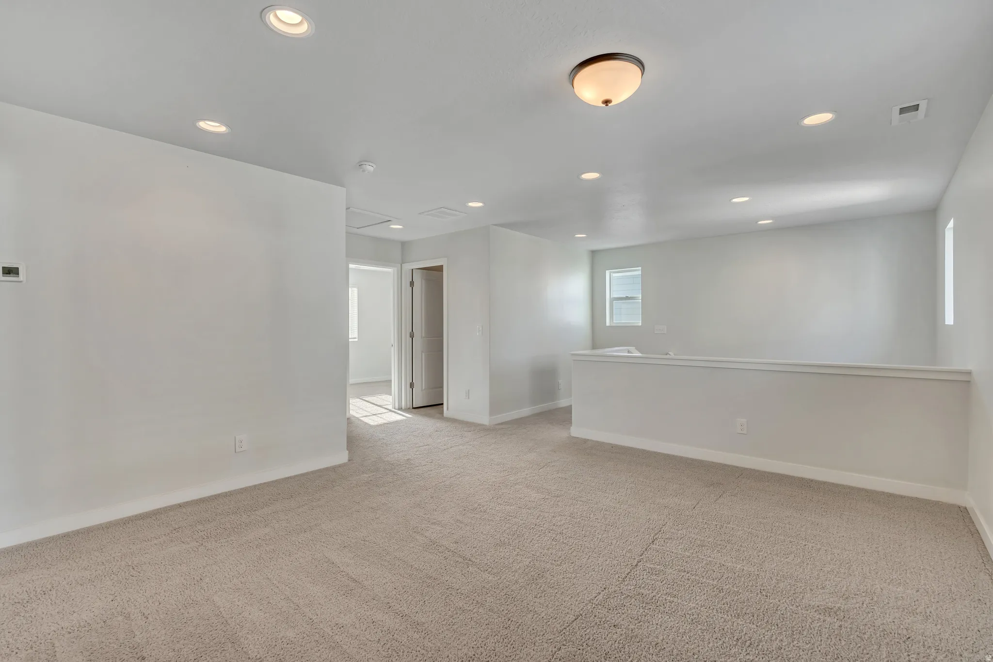 Spacious upstairs loft area featuring neutral-toned carpeting, white walls, and a combination of recessed and flush-mount ceiling lighting