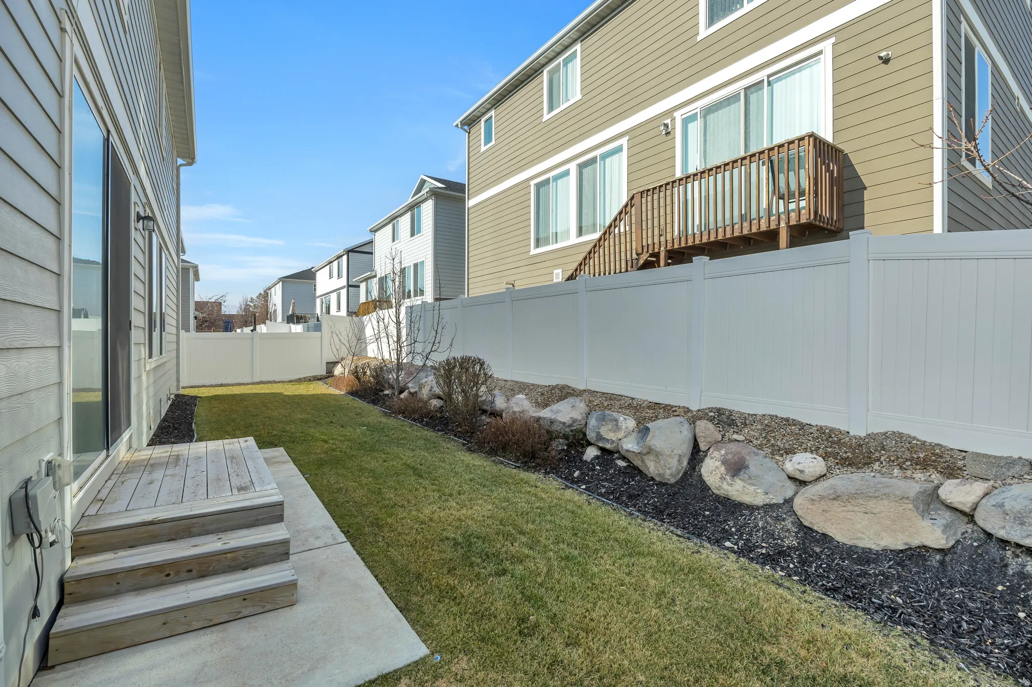 Backyard featuring a wooden deck with steps, an adjacent concrete patio, and a manicured lawn