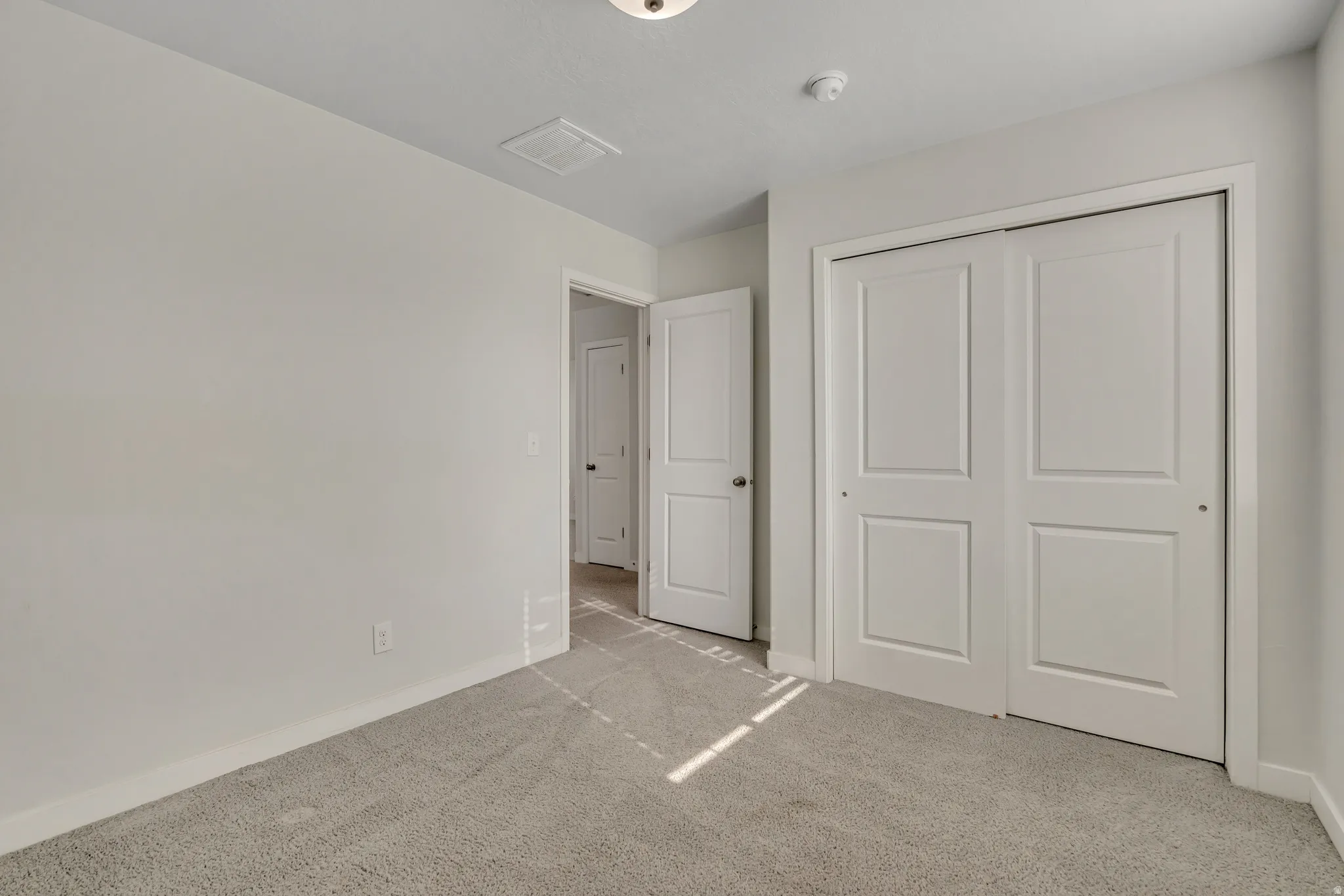 Neutral wall paint throughout a carpeted room featuring a double-door closet with panel detailing