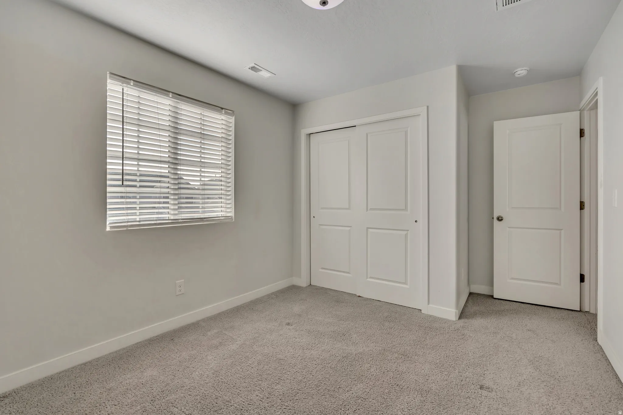 Spacious room featuring neutral carpeting, light gray wall paint, and white trim