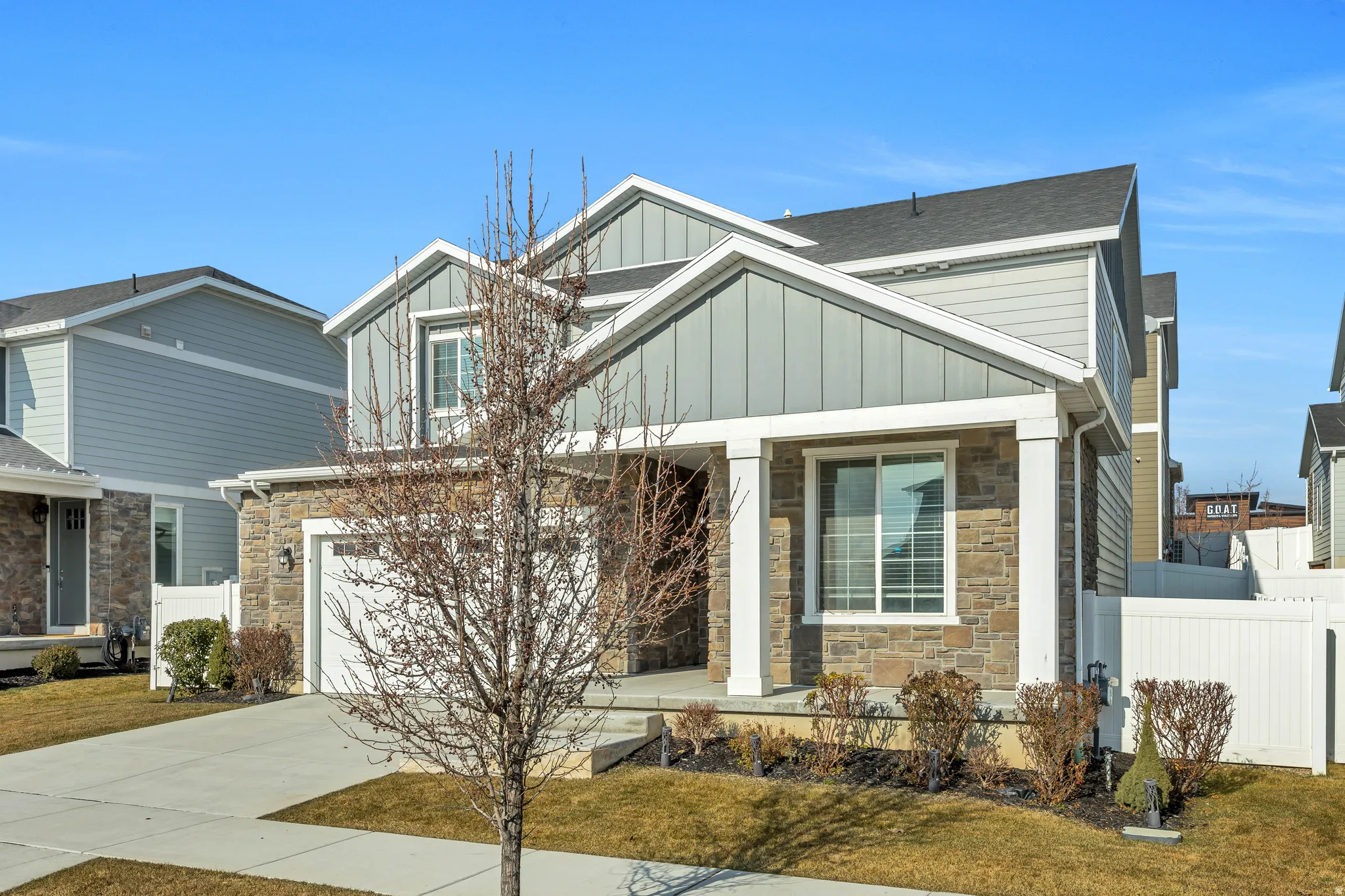 Modern two-story residence featuring a stone and siding exterior, an attached garage, a covered front porch, and mature landscaping