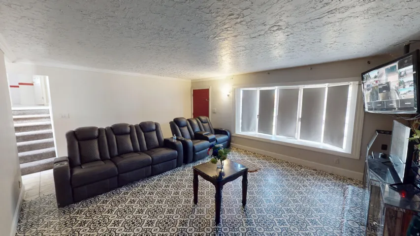 Living area featuring patterned tile flooring, a multi-pane window with roller shades, and a textured ceiling