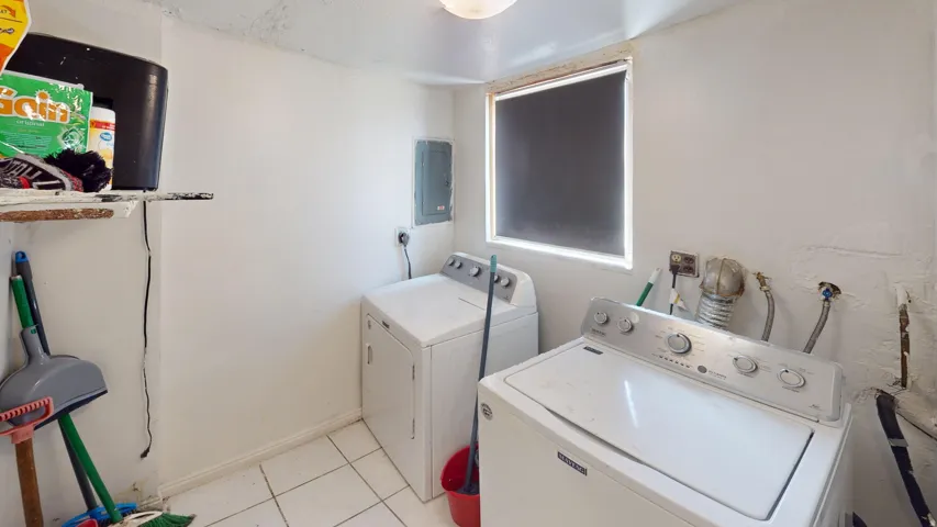 Dedicated laundry area featuring white tile flooring, a window with a roller shade, and an electrical panel