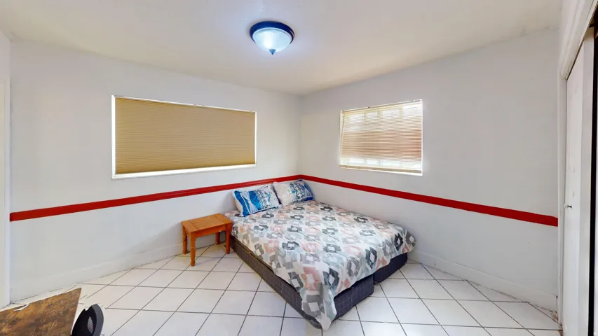 Room featuring white tile flooring, two windows with blinds, a red accent band on the walls, and a ceiling-mounted light fixture