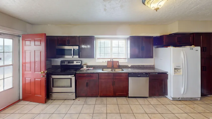 Kitchen featuring dark wood cabinetry, granite-style countertops, and stainless steel appliances including a microwave, range, and dishwasher