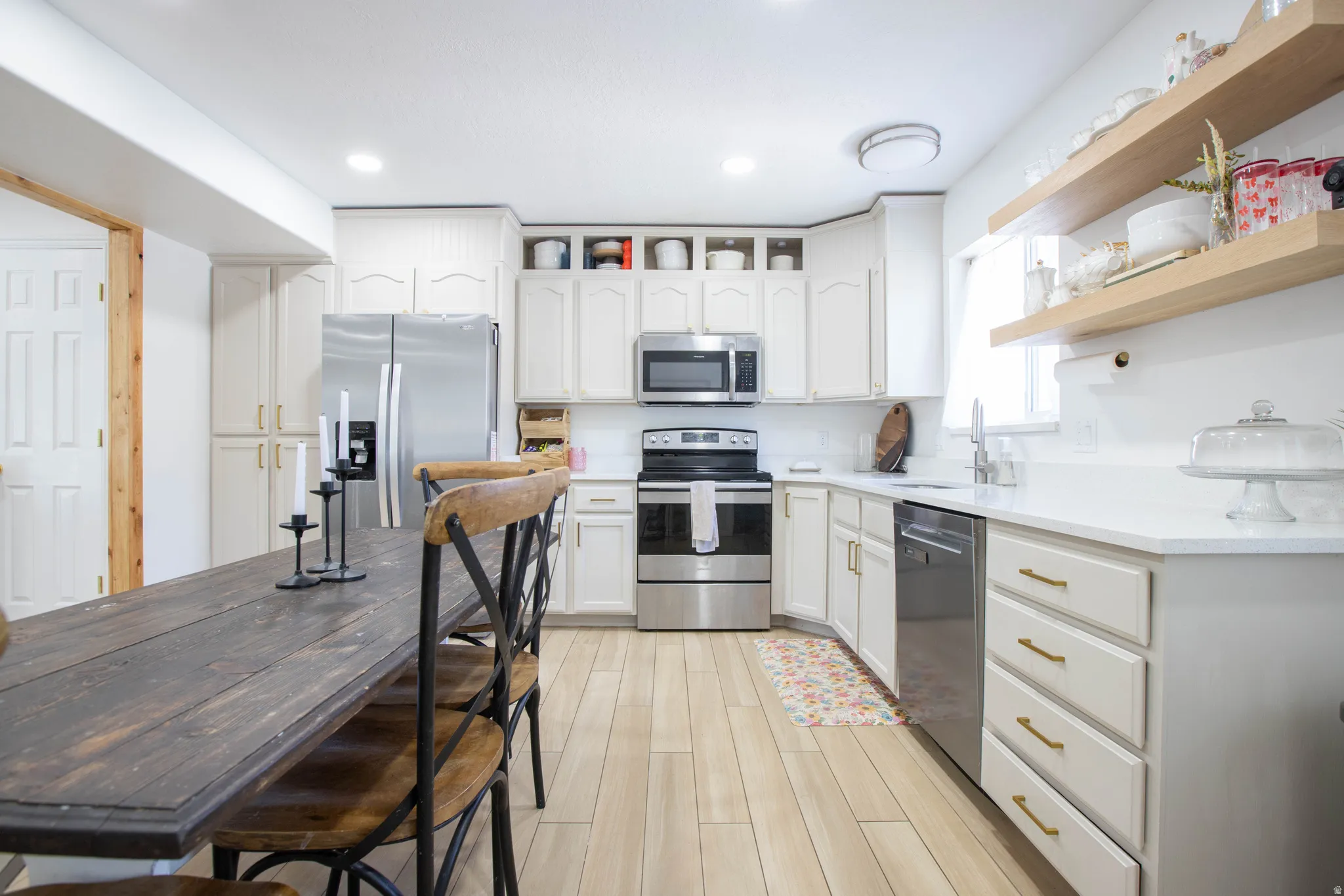 Modern kitchen featuring light-toned cabinetry with gold-finish hardware, stainless steel appliances, a white tile backsplash, and light wood-finish flooring