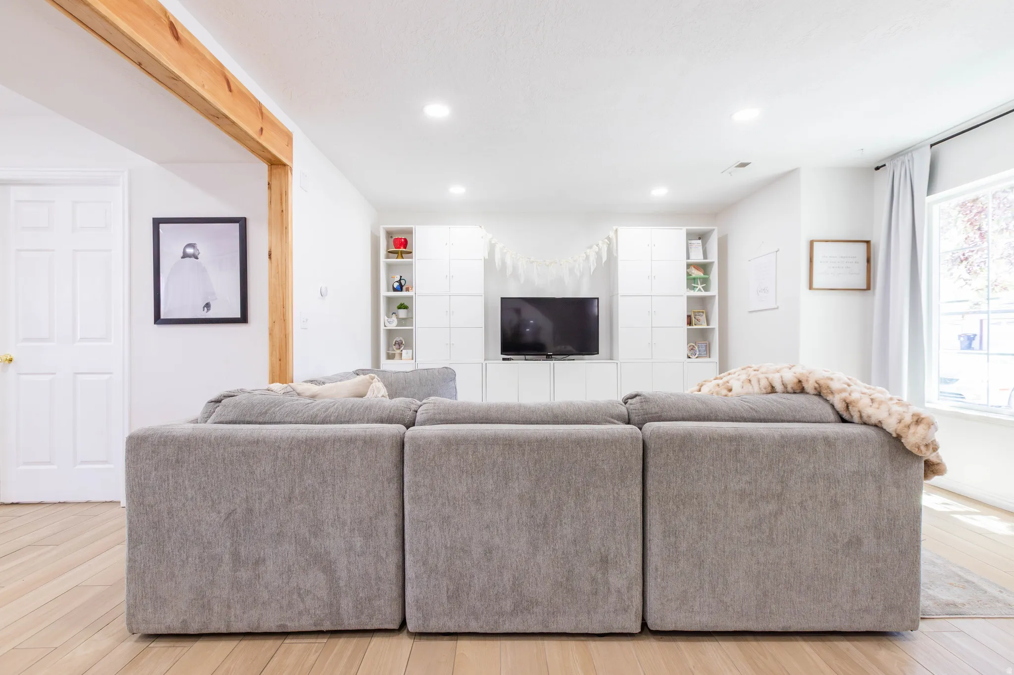 Open living area featuring wood-finish flooring, a wood beam accent, recessed lighting, and a window with natural light