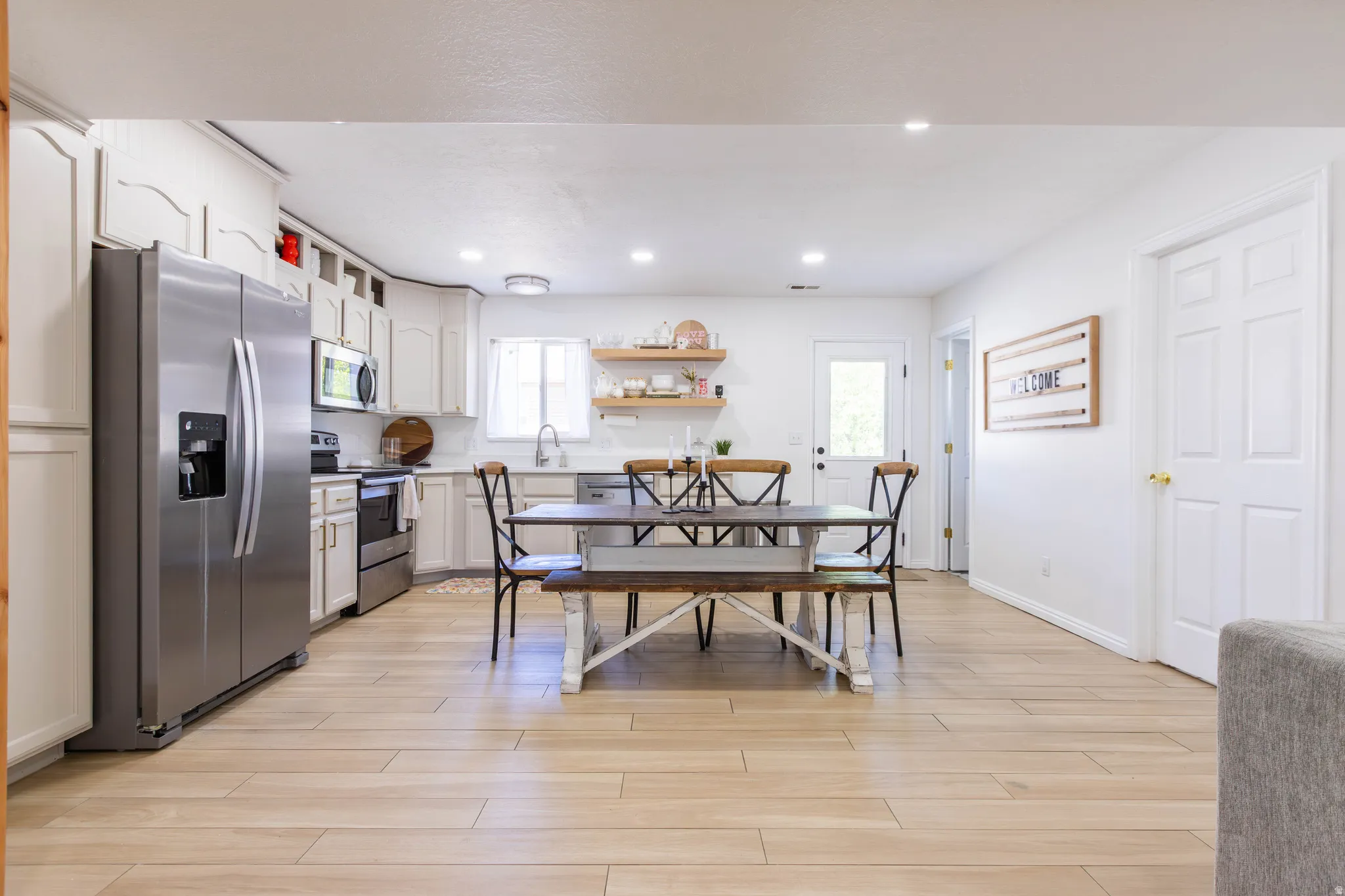 Open-concept kitchen and dining area featuring light-toned wood-finish flooring, white cabinetry, and stainless steel appliances