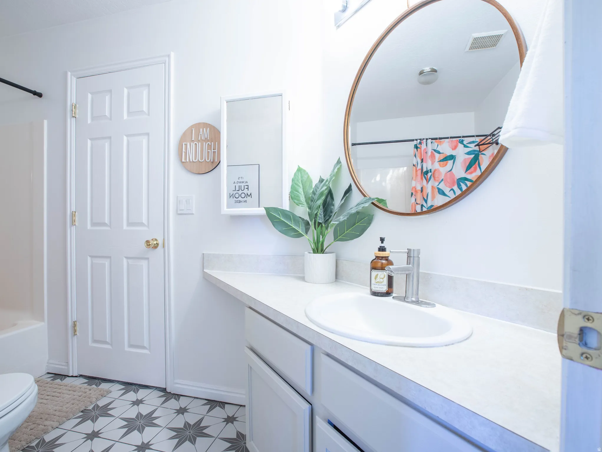 Contemporary bathroom featuring a white vanity with an integrated sink, a large oval mirror with a wood-finish frame, and patterned floor tiling