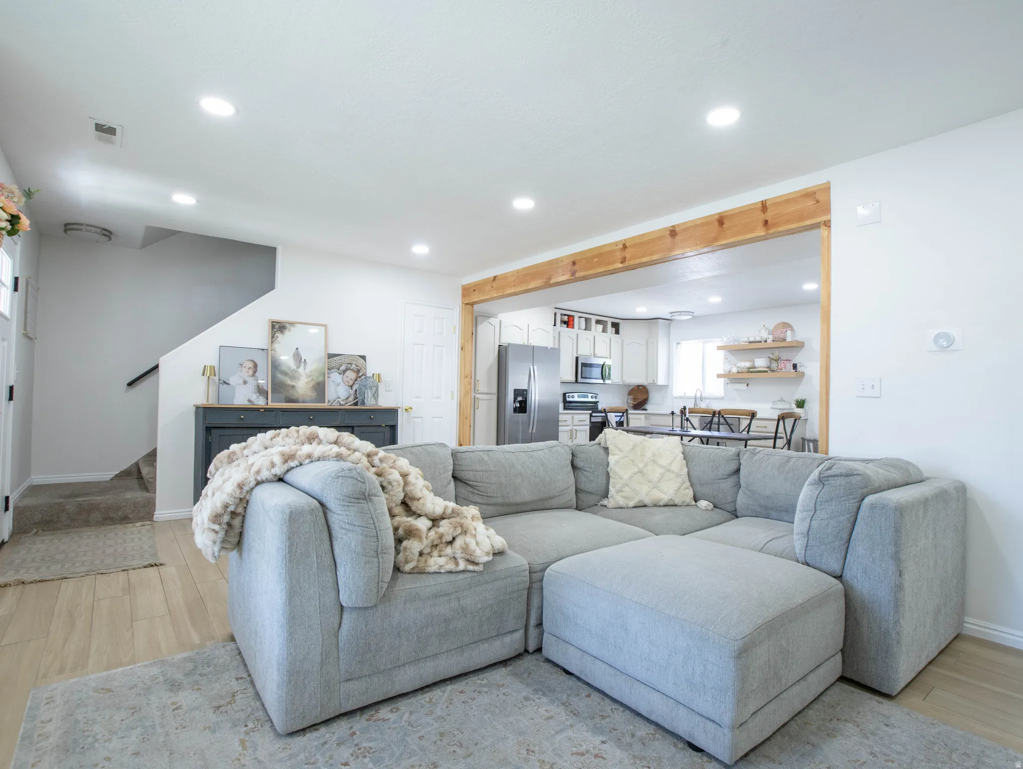 Open-concept living space featuring wood-finish flooring, recessed lighting, and a broad cased opening with a timber beam accent