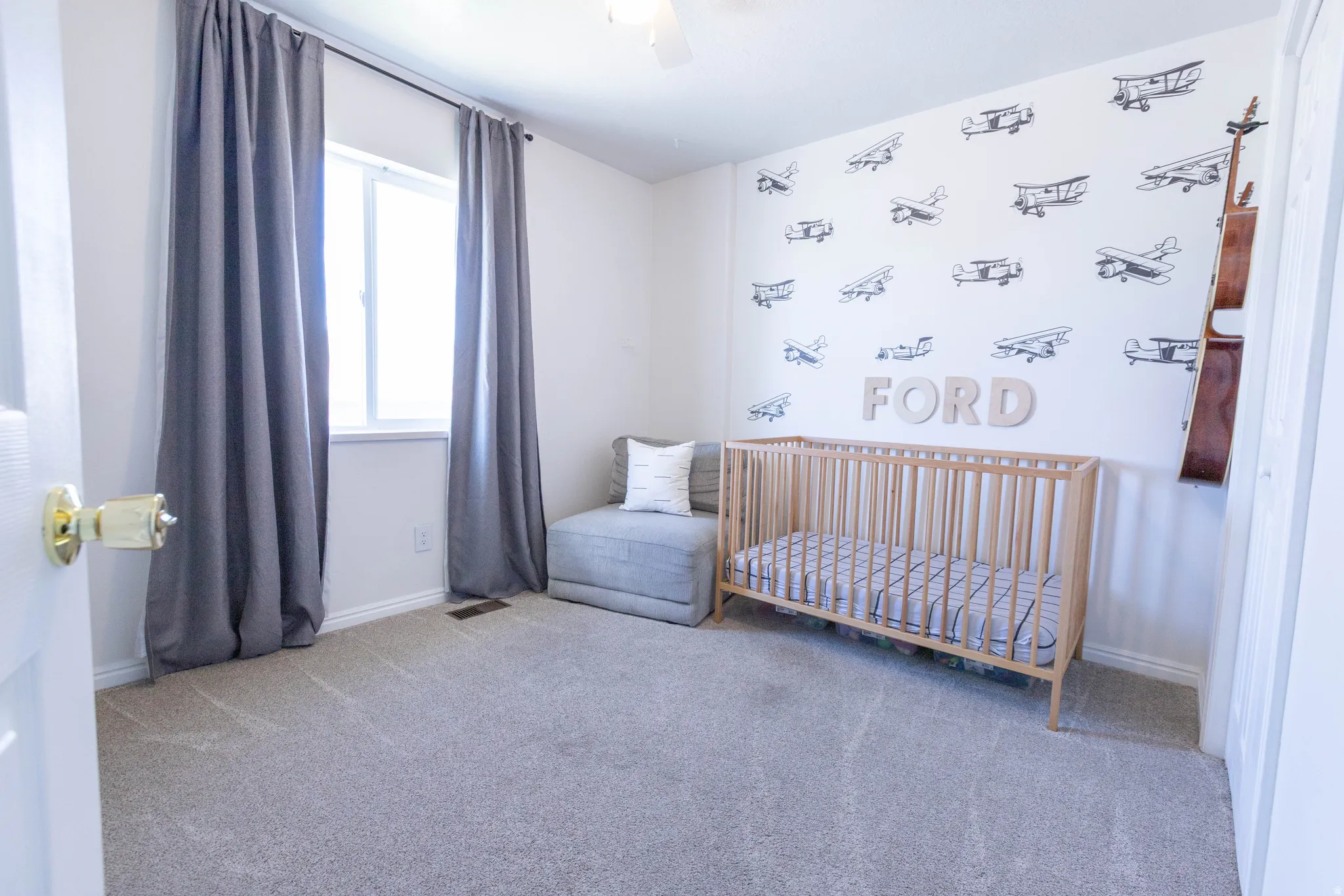 Carpeted room featuring a window with gray drapes, light-toned walls, and a ceiling fan