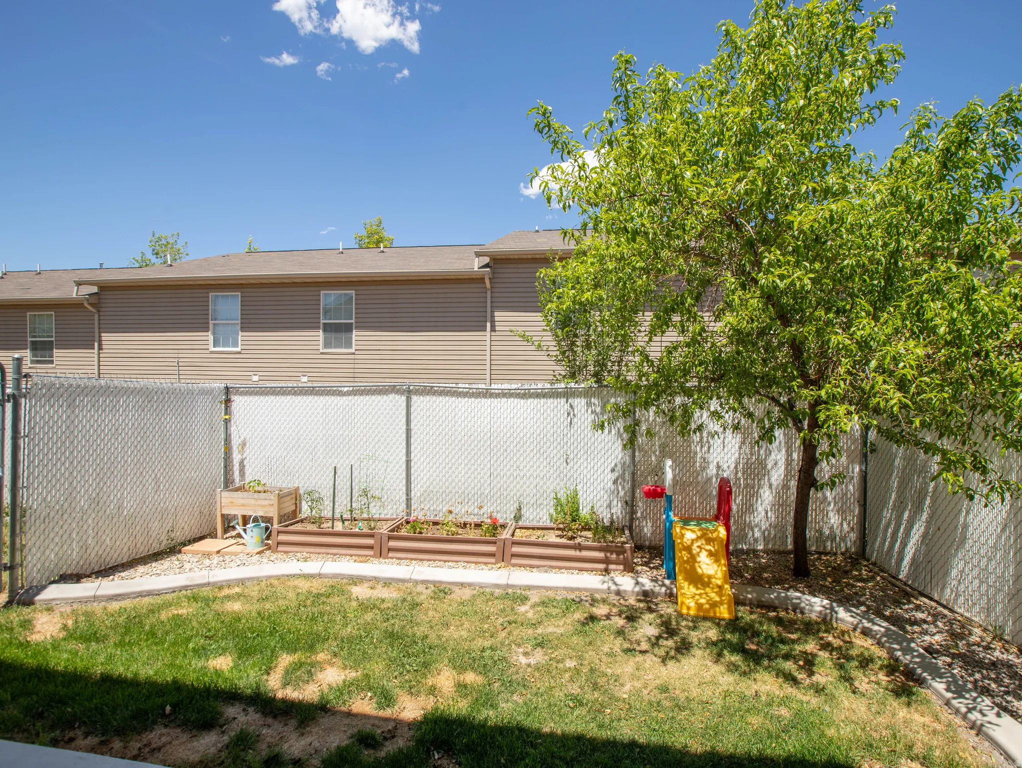 Fenced backyard featuring a mature tree, two raised garden beds, and a chain link fence