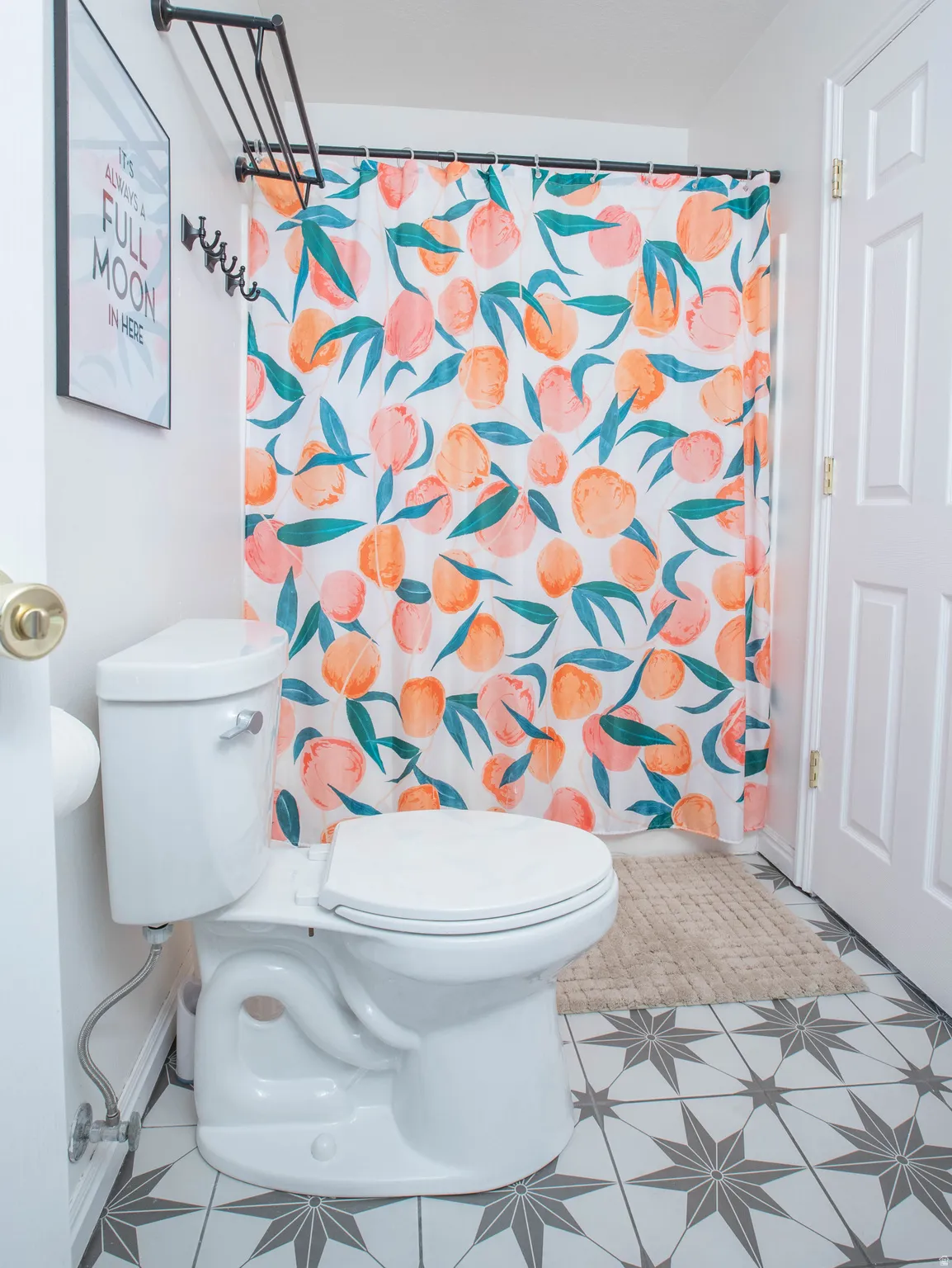 Bathroom featuring geometric star-patterned floor tiles, a white toilet with a chrome flush lever, and a white interior door with a brass-finish doorknob