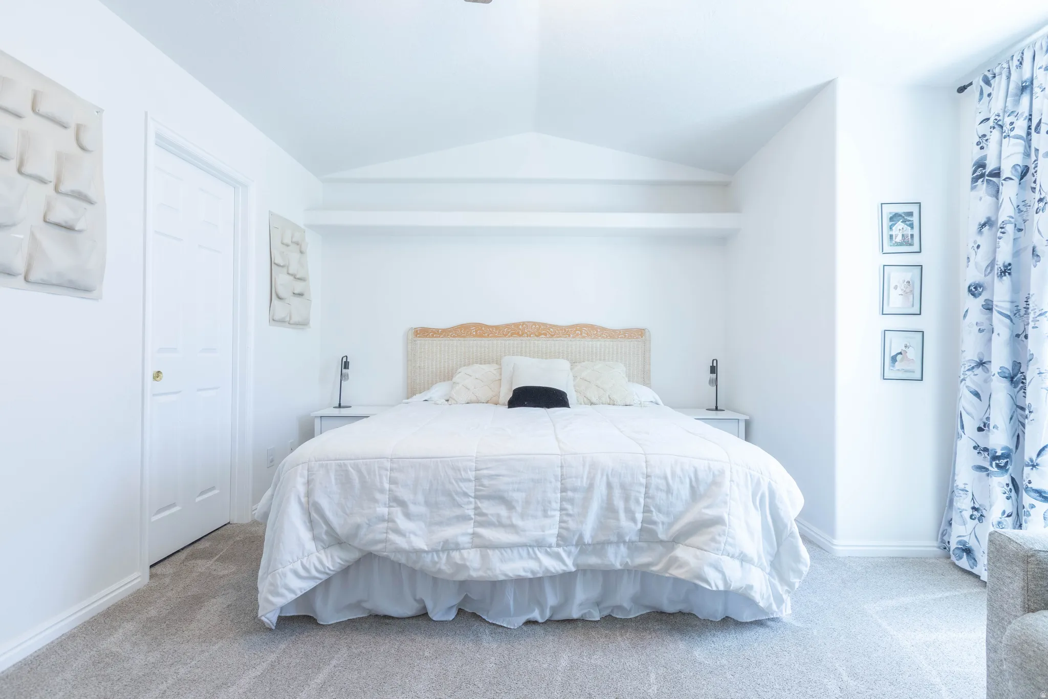 Carpeted bedroom featuring a vaulted ceiling with decorative ledges, a paneled door, and a window with patterned drapes
