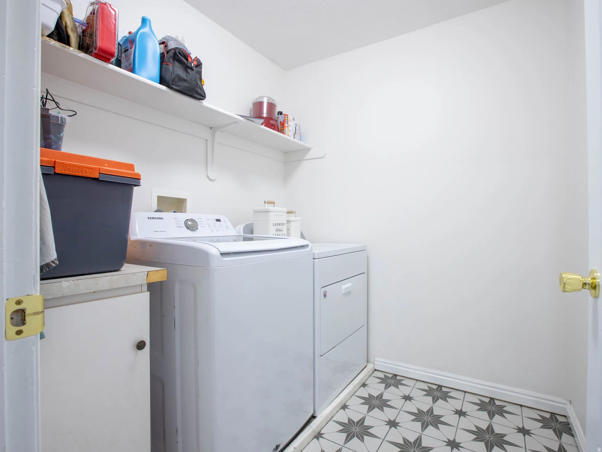 Laundry area featuring patterned floor tiles, white walls, and built-in shelving