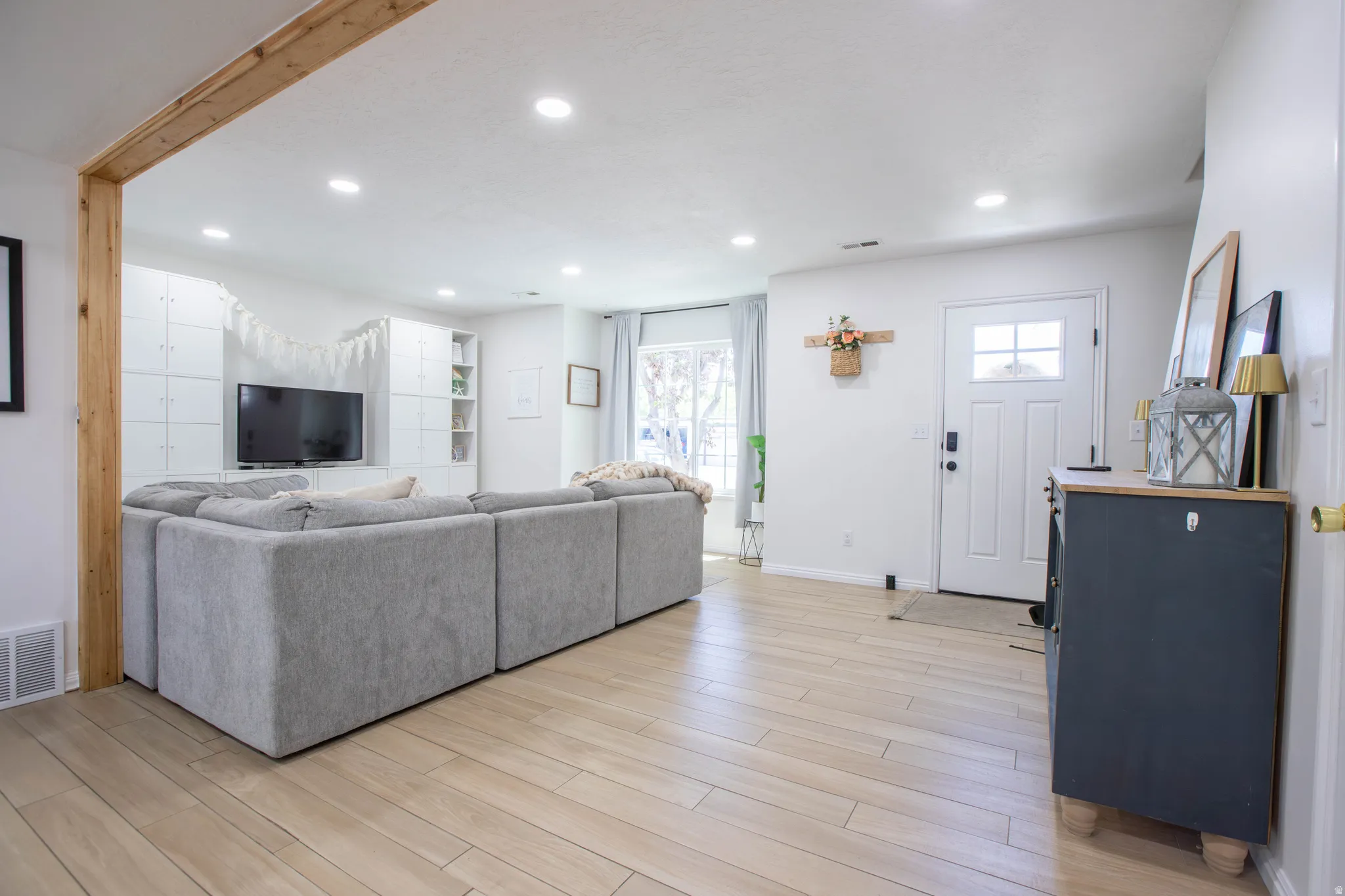 Open-concept living space featuring light wood-finish flooring, recessed lighting, and a white paneled accent wall with built-in shelving