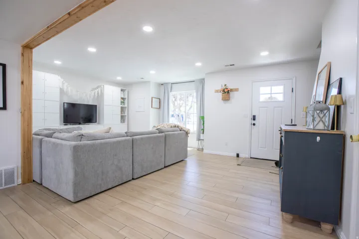 Open-concept living space featuring light wood-finish flooring, recessed lighting, and a white paneled accent wall with built-in shelving