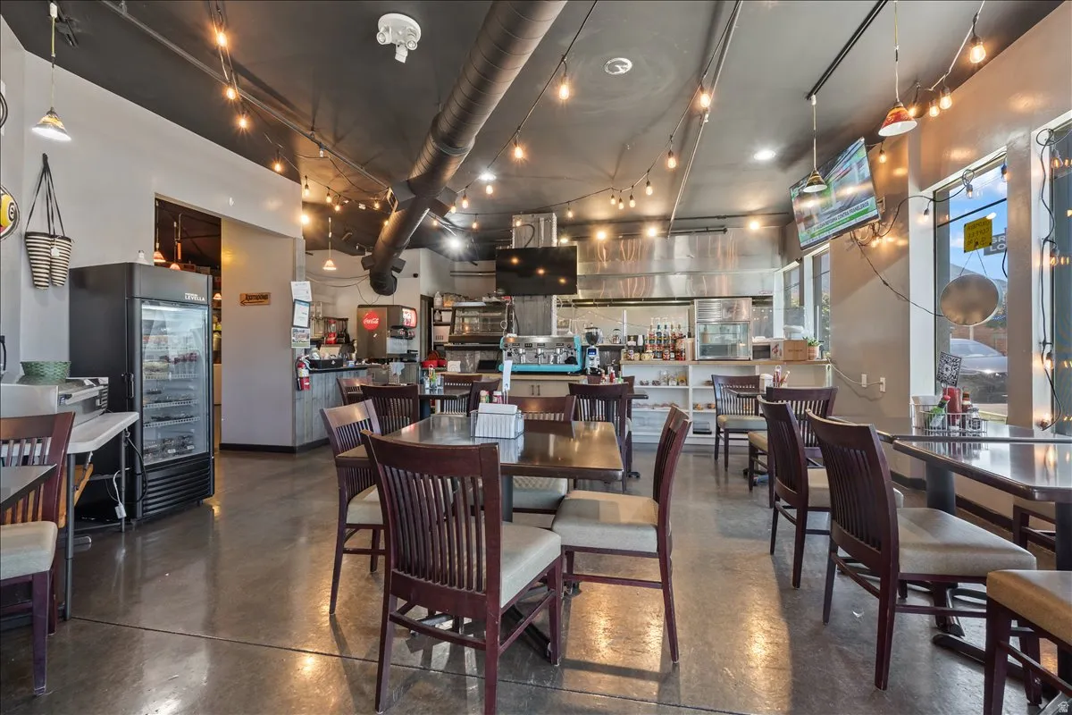 Open-concept dining area featuring polished concrete flooring, exposed overhead ductwork, and string lighting