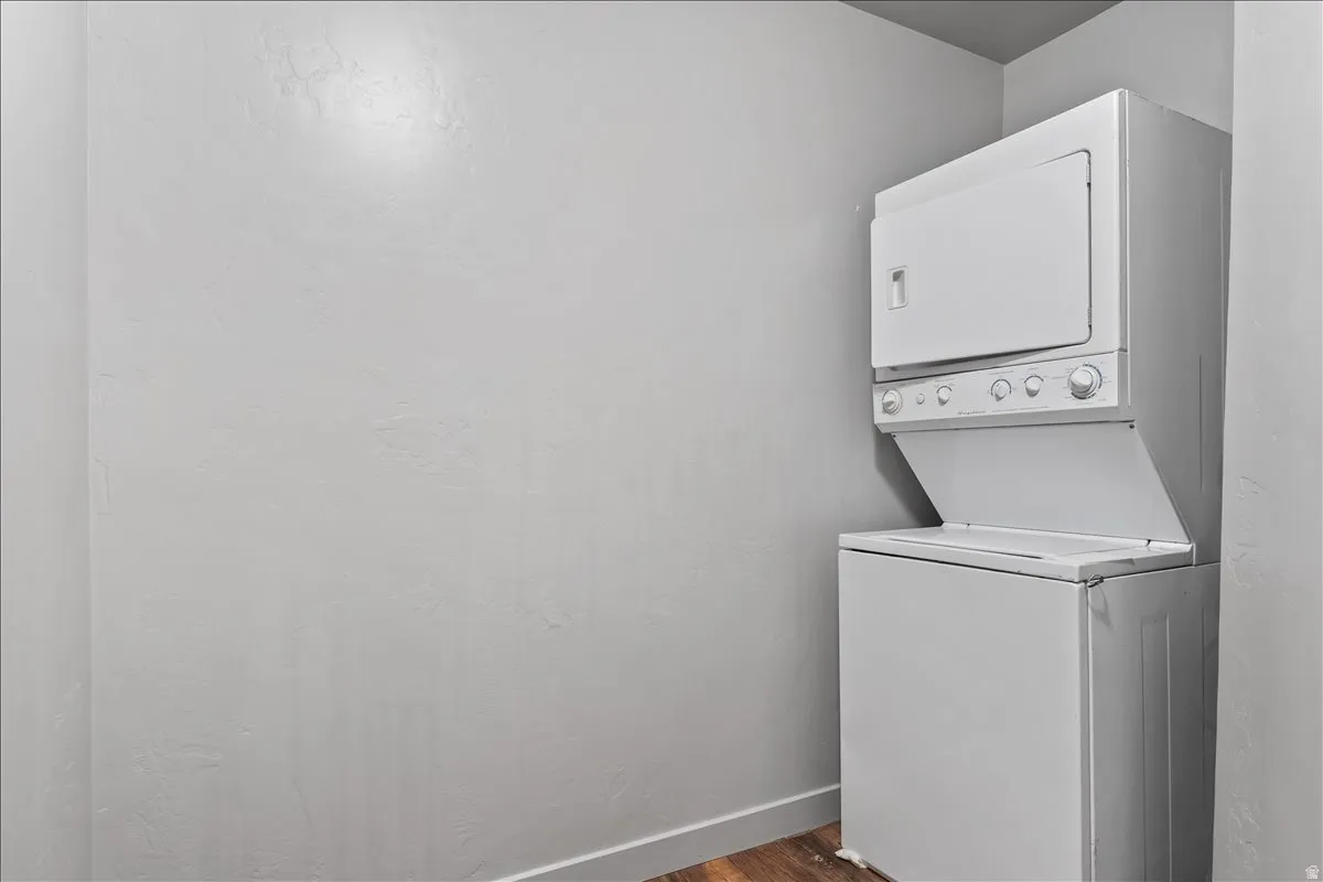 Dedicated laundry area featuring a white stacked washer and dryer unit, contemporary gray wall finish, white baseboard trim, and wood-finish flooring