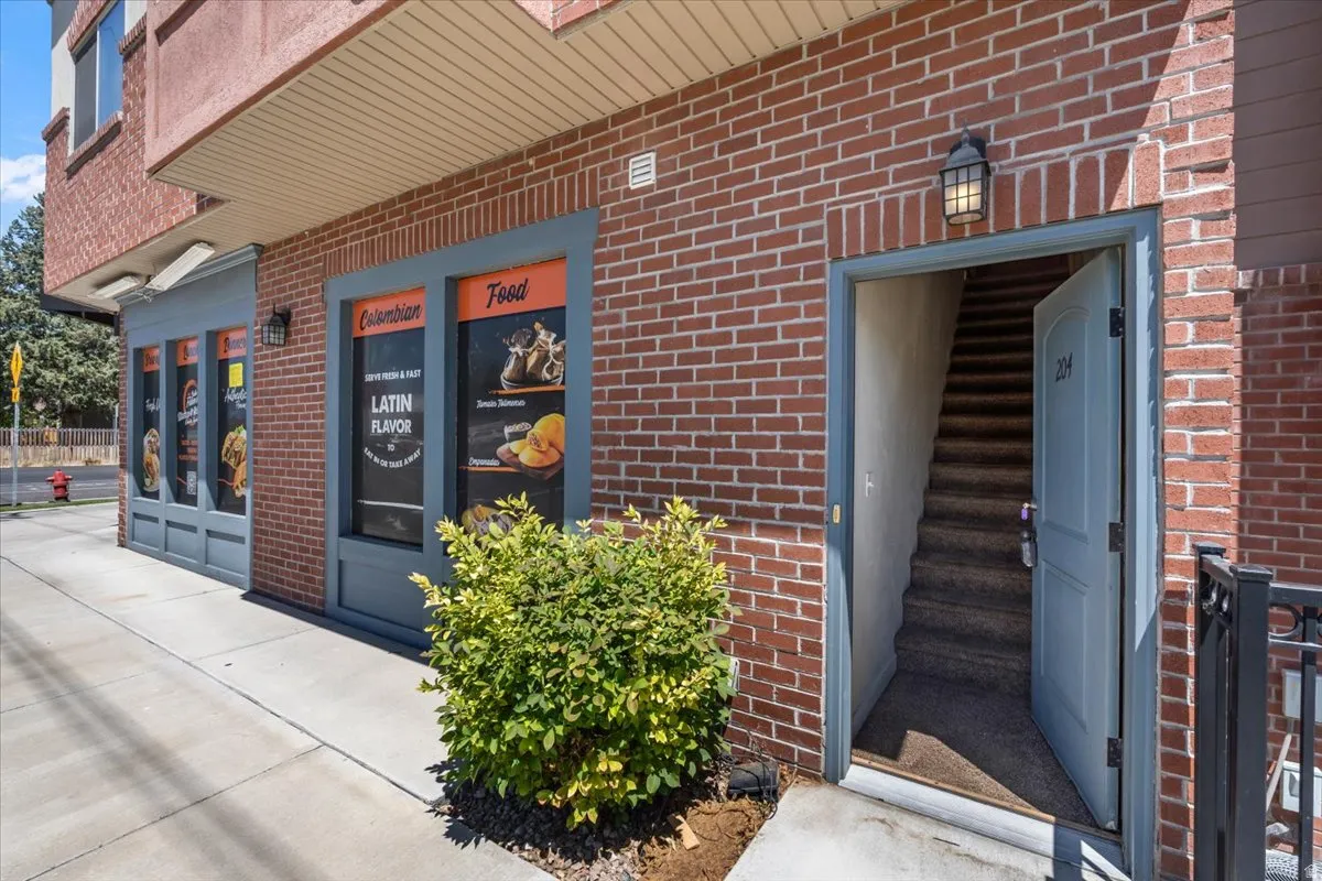 Brick exterior with large storefront windows and a separate entrance featuring an open door with visible stairs