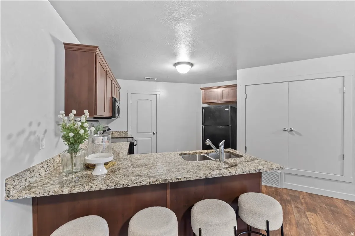 Kitchen featuring an island with a double basin sink and granite-style countertop, dark wood-finish cabinetry, black appliances, and wood-finish flooring