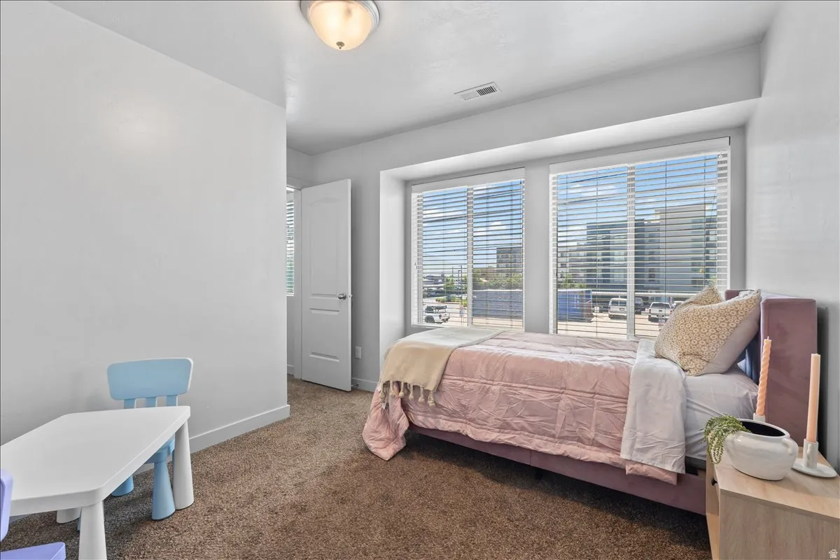 Carpeted bedroom featuring large windows with horizontal blinds, providing ample natural light