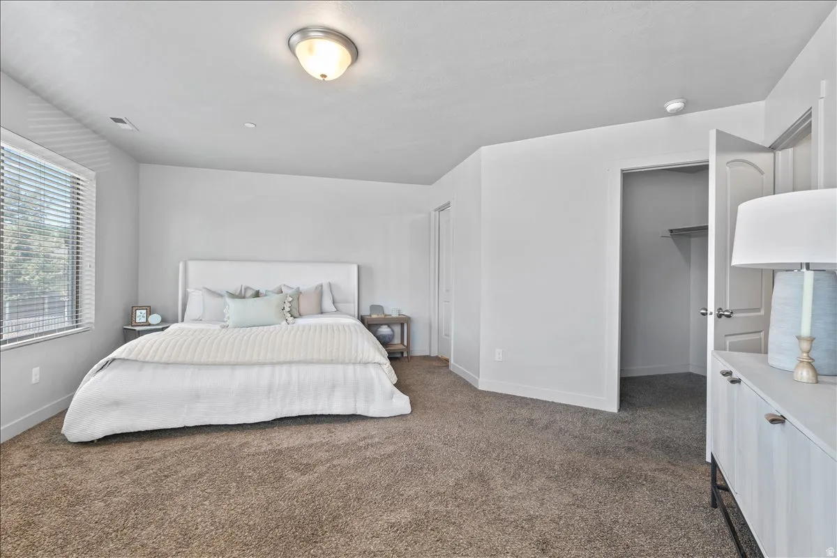 Carpeted bedroom featuring a large window with horizontal blinds, a ceiling-mounted light fixture, white walls, and a closet with a white panel door