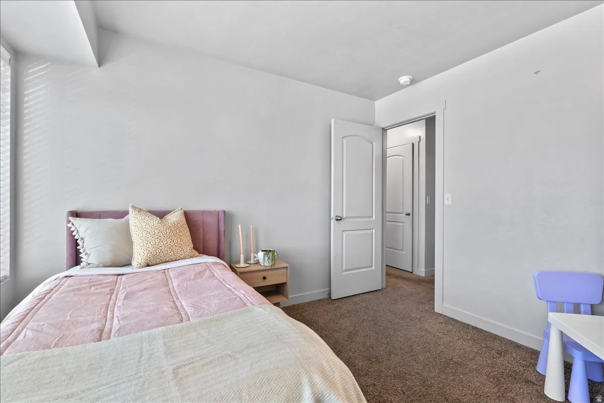 Light-filled room featuring neutral wall paint, carpet flooring, a single window with blinds, and white interior doors with contemporary hardware