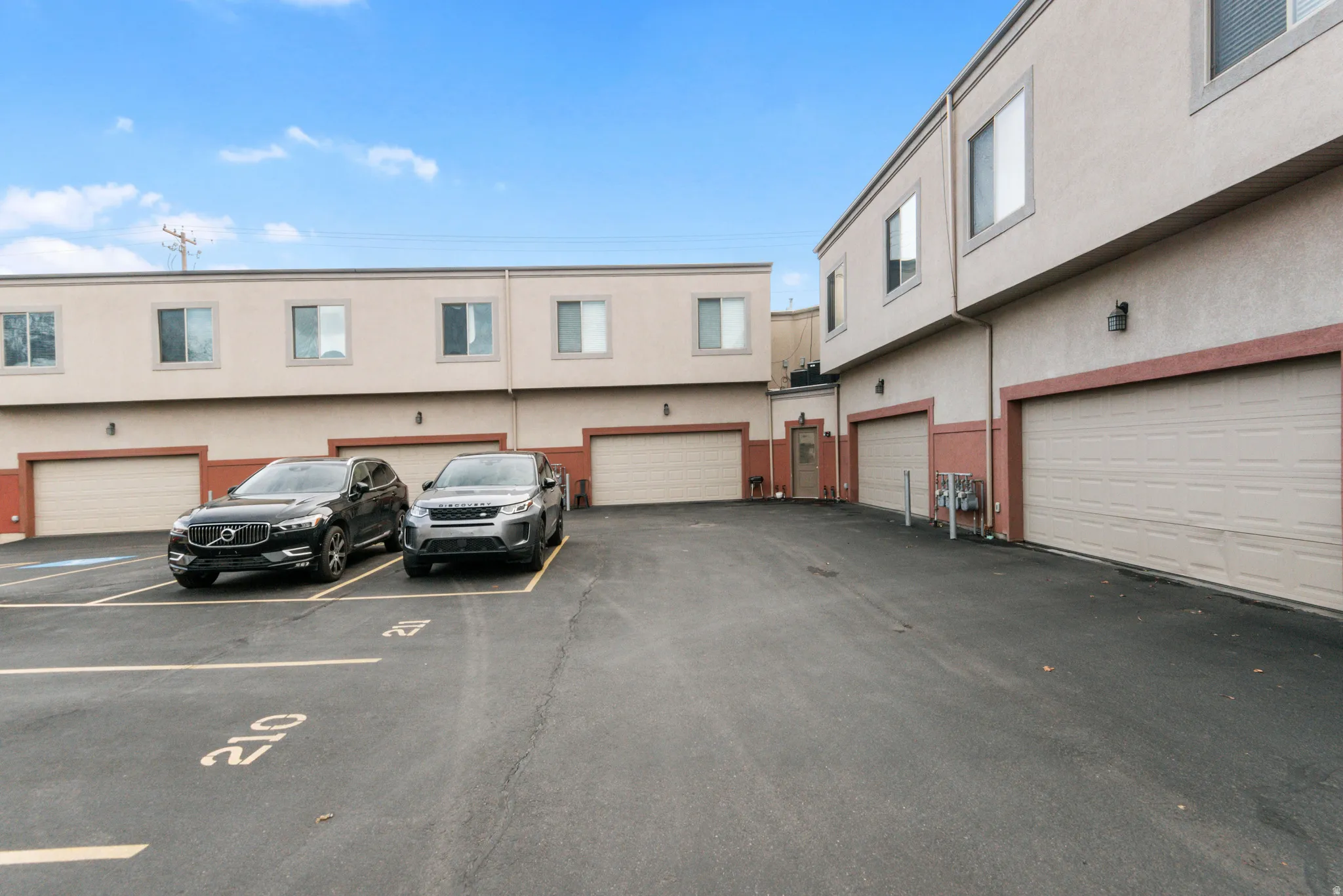 Multi-story building exterior featuring light-colored stucco siding with red-brown trim accents