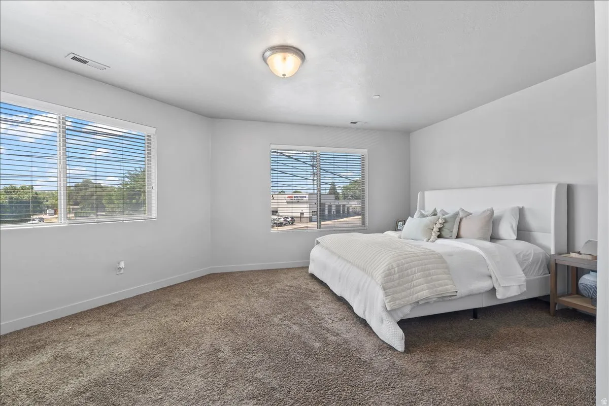 Spacious room featuring multiple windows with horizontal blinds, neutral wall paint, and a textured carpeted floor