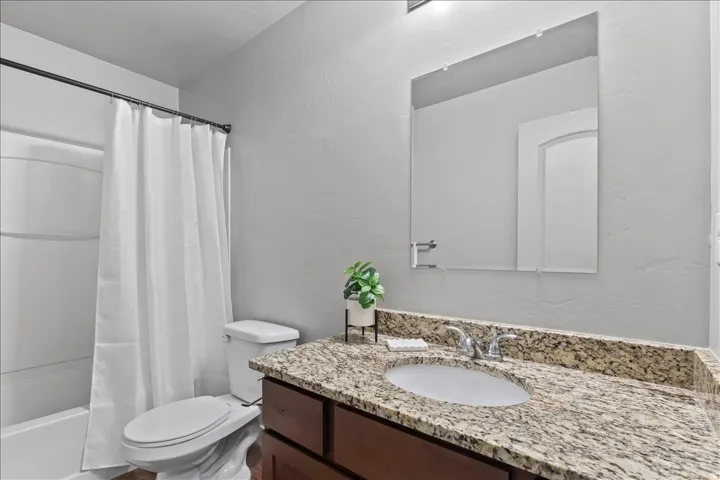 Bathroom featuring a wood-finish vanity with a granite countertop, undermount sink, and chrome faucet