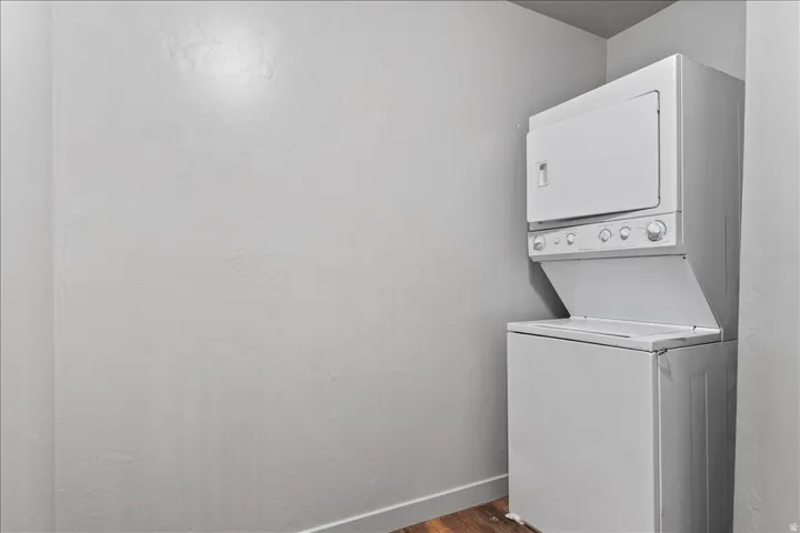 Dedicated laundry area featuring a white stacked washer and dryer unit, contemporary gray wall finish, white baseboard trim, and wood-finish flooring