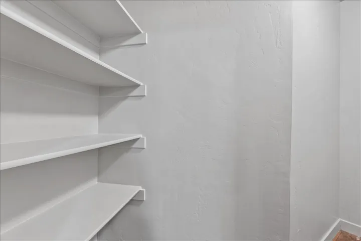 Built-in shelving unit with multiple white shelves against a textured wall