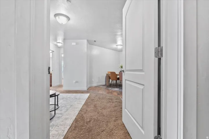 Interior hallway with white walls and trim, overhead flush-mount lighting, and mixed flooring featuring brown carpet and wood-finish flooring