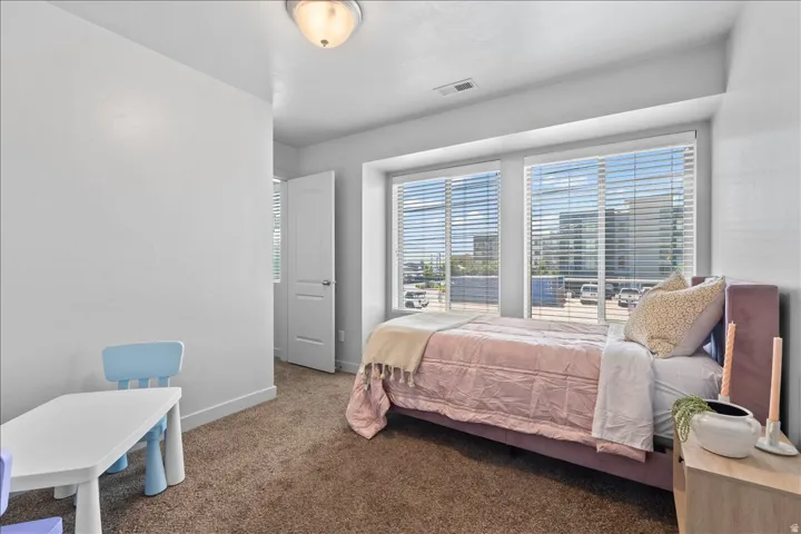 Carpeted bedroom featuring large windows with horizontal blinds, providing ample natural light