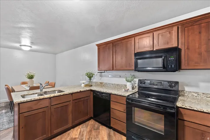 Kitchen featuring wood-finish cabinetry, granite-style countertops, and a full suite of black appliances, including an oven/range, microwave, and dishwasher