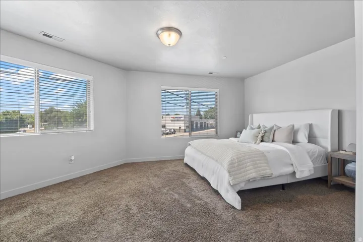 Spacious room featuring multiple windows with horizontal blinds, neutral wall paint, and a textured carpeted floor