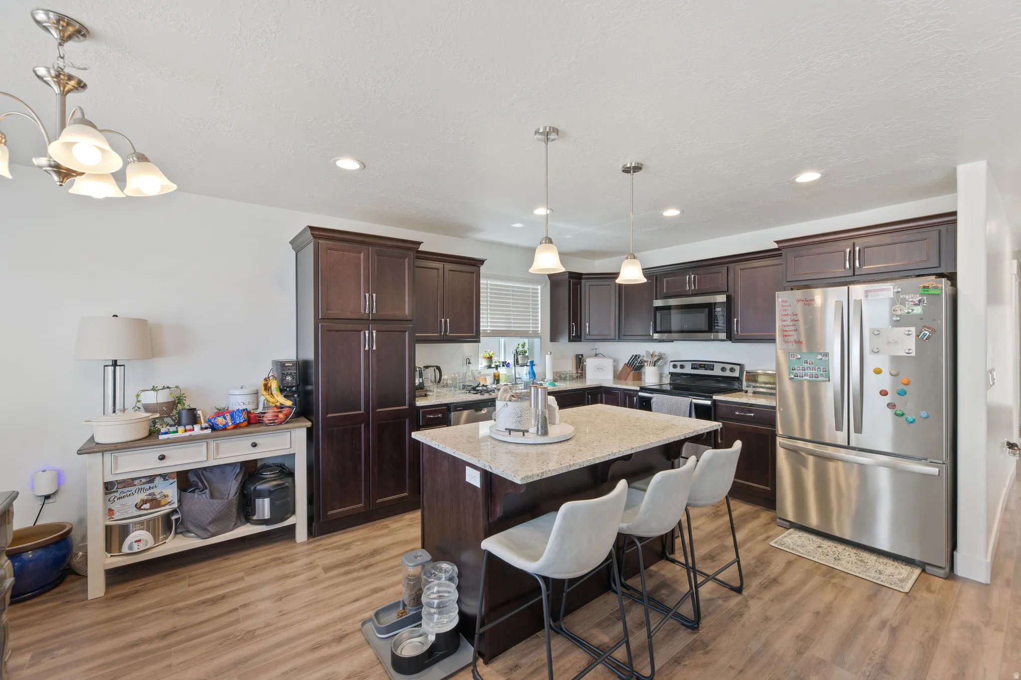 Open-concept kitchen featuring wood-finish flooring, dark wood cabinetry, a central island with a light-colored countertop, and stainless steel appliances