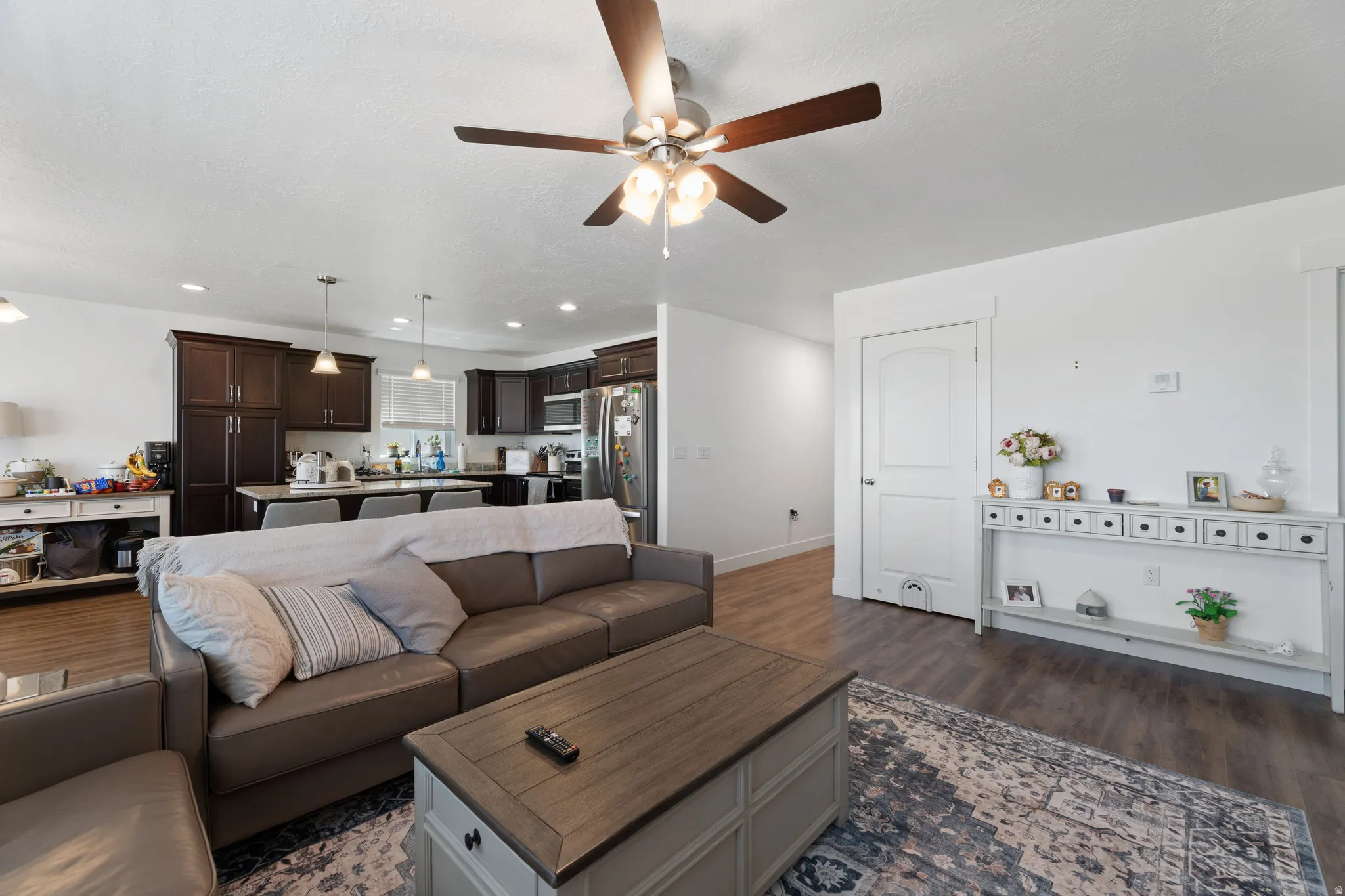 Spacious living area featuring wood-finish flooring, a ceiling fan with integrated lighting, and an open concept layout connecting to the kitchen