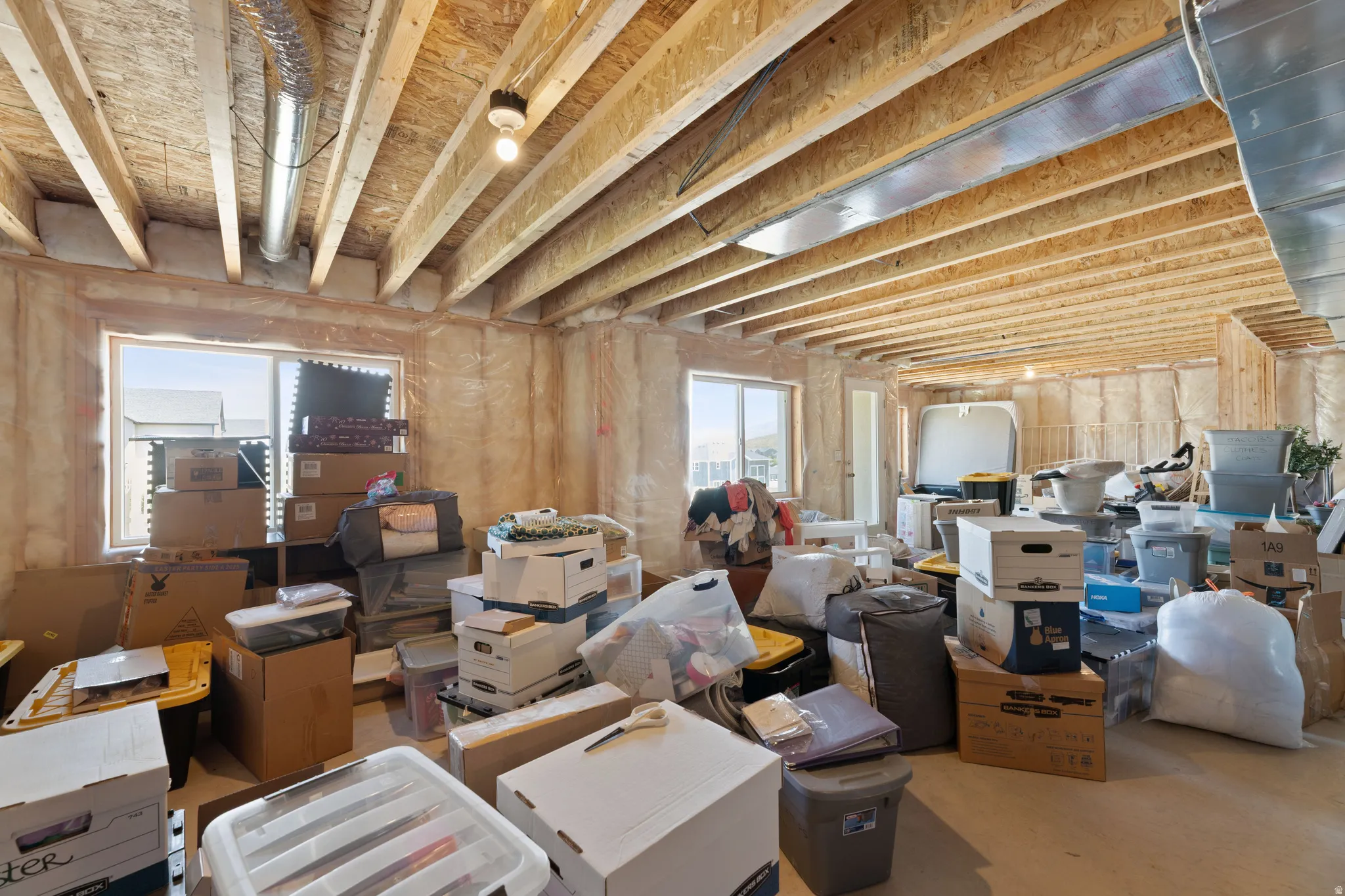 Unfinished basement space featuring exposed wood joists, structural support beams, and two windows