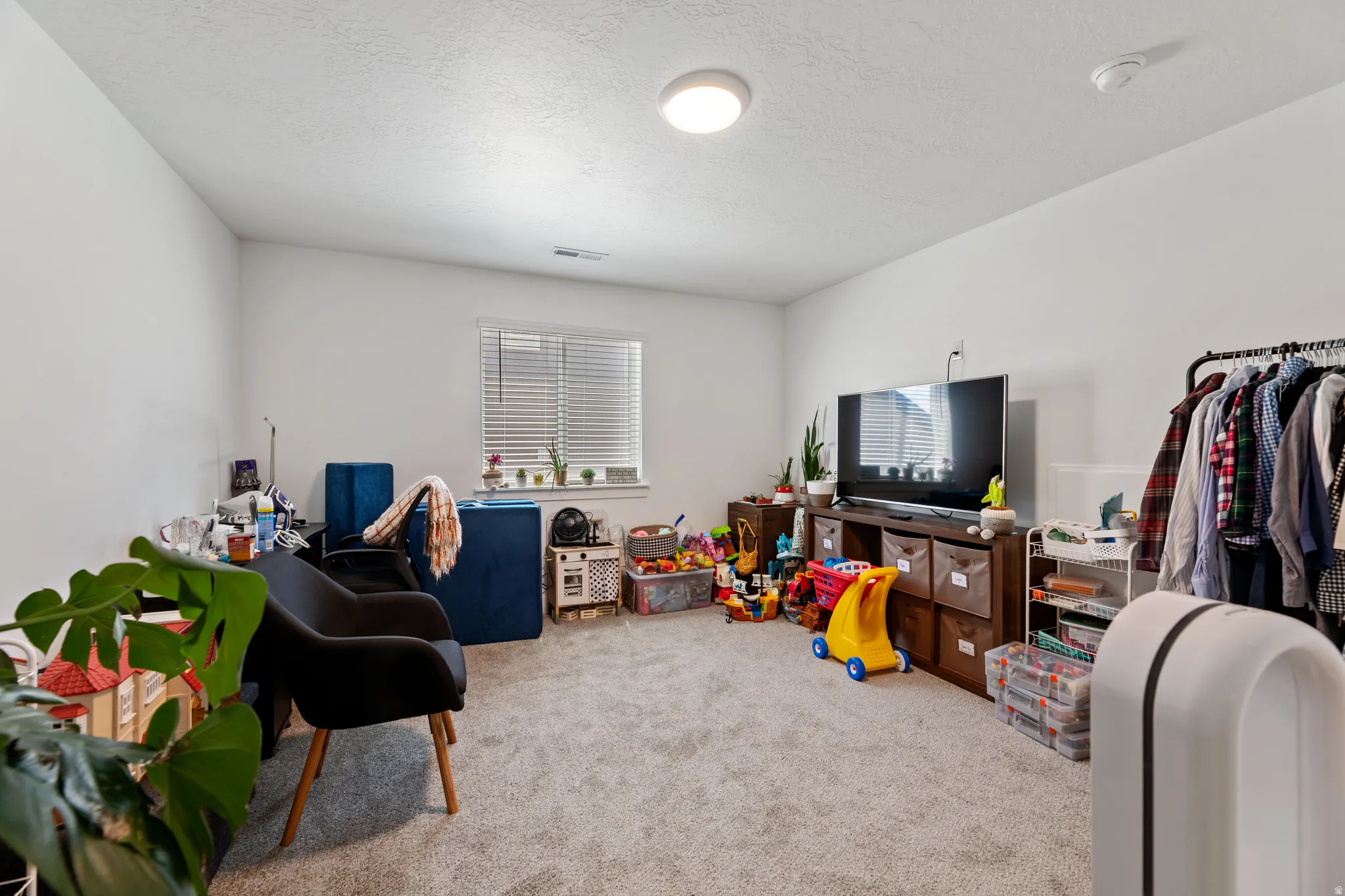 Carpeted room featuring a single window with blinds, white walls, and a ceiling-mounted light fixture