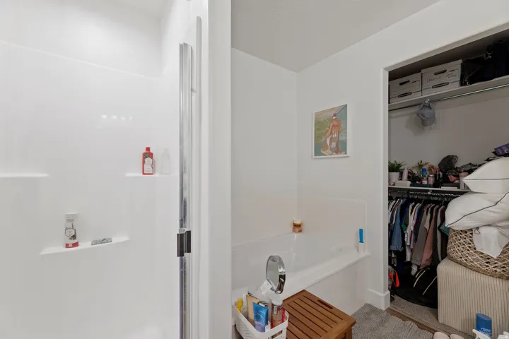 White shower enclosure with built-in shelving, glass shower door, and an adjacent built-in bathtub