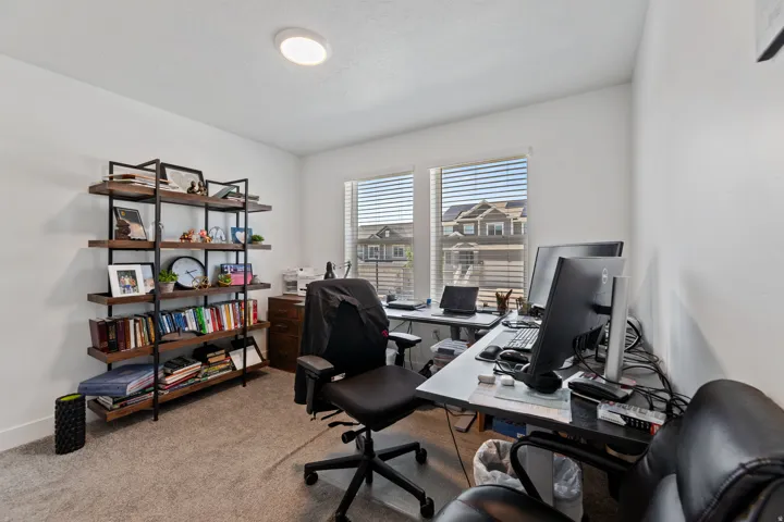 Dedicated workspace featuring two large windows, recessed ceiling lighting, wall-to-wall carpeting, and a built-in shelving unit with dark wood-finish shelves and a black metal frame