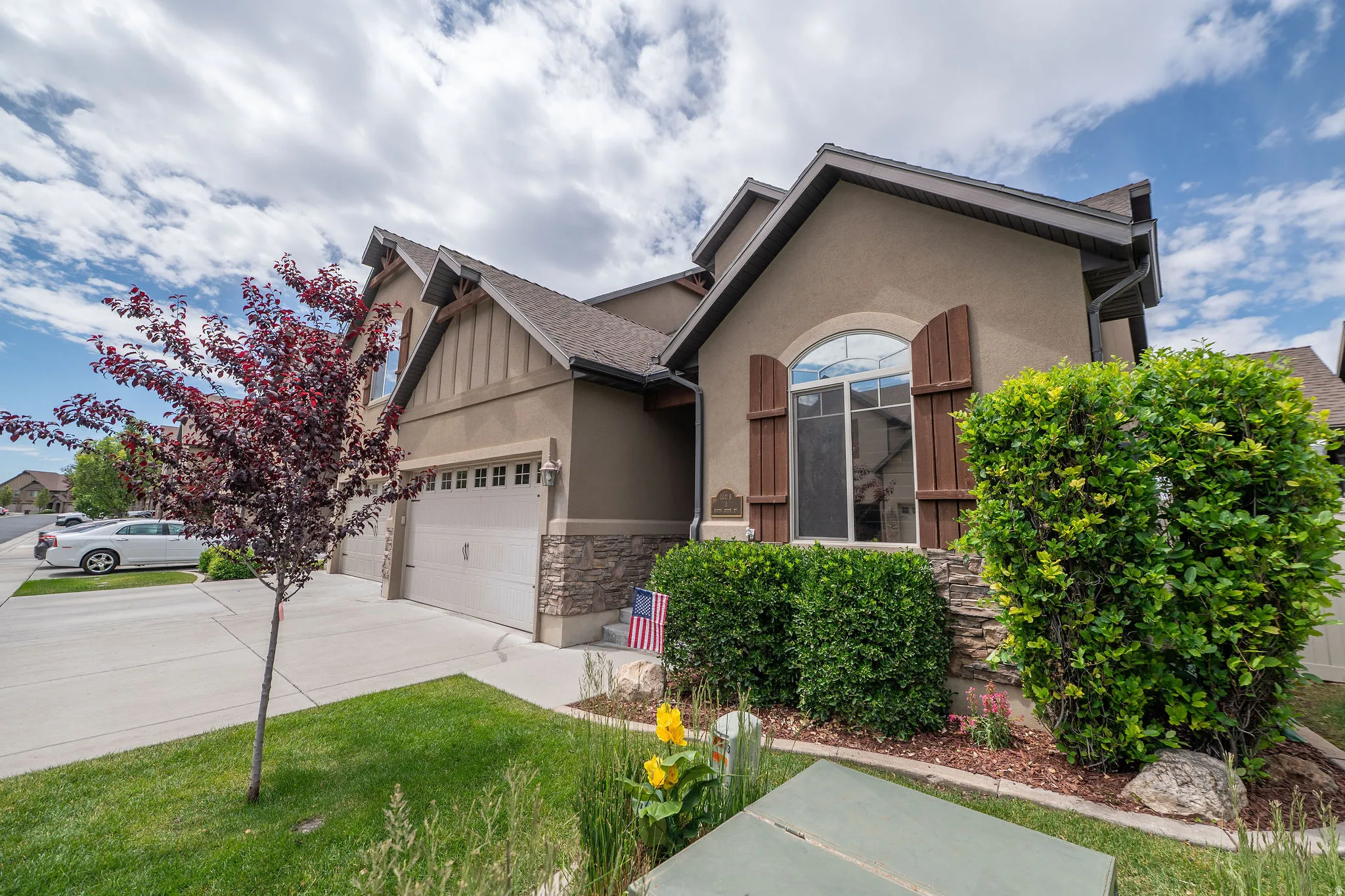 Charming front elevation angle highlighting the craftsman roofline, board-and-batten siding, wood shutters, ornamental plum tree, and stacked stone base. This home photographs beautifully from every angle.