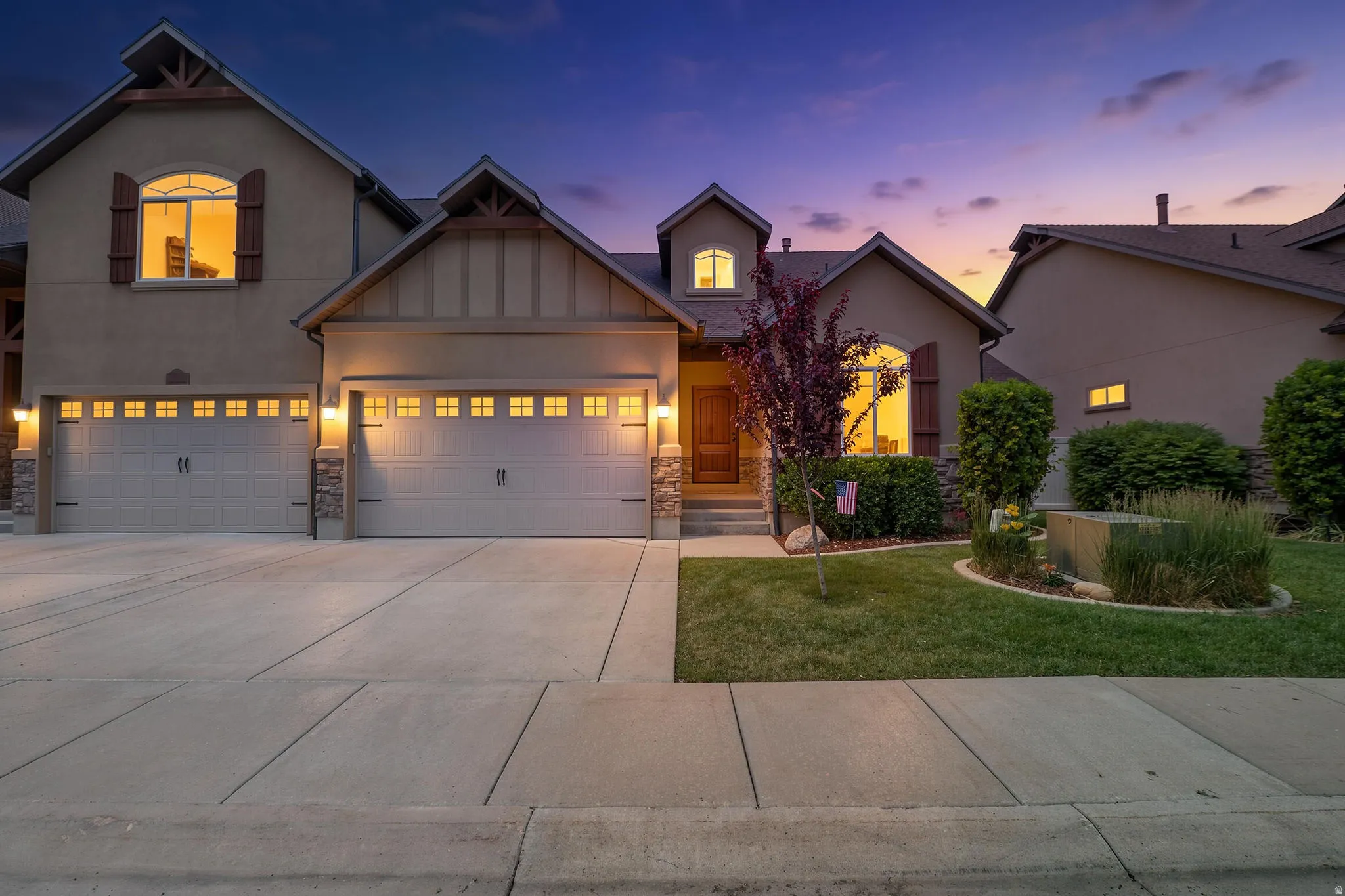 Jaw-dropping twilight curb appeal with craftsman details, stacked stone accents, 2-car garage, and warm glowing windows set against a stunning Utah sunset sky.