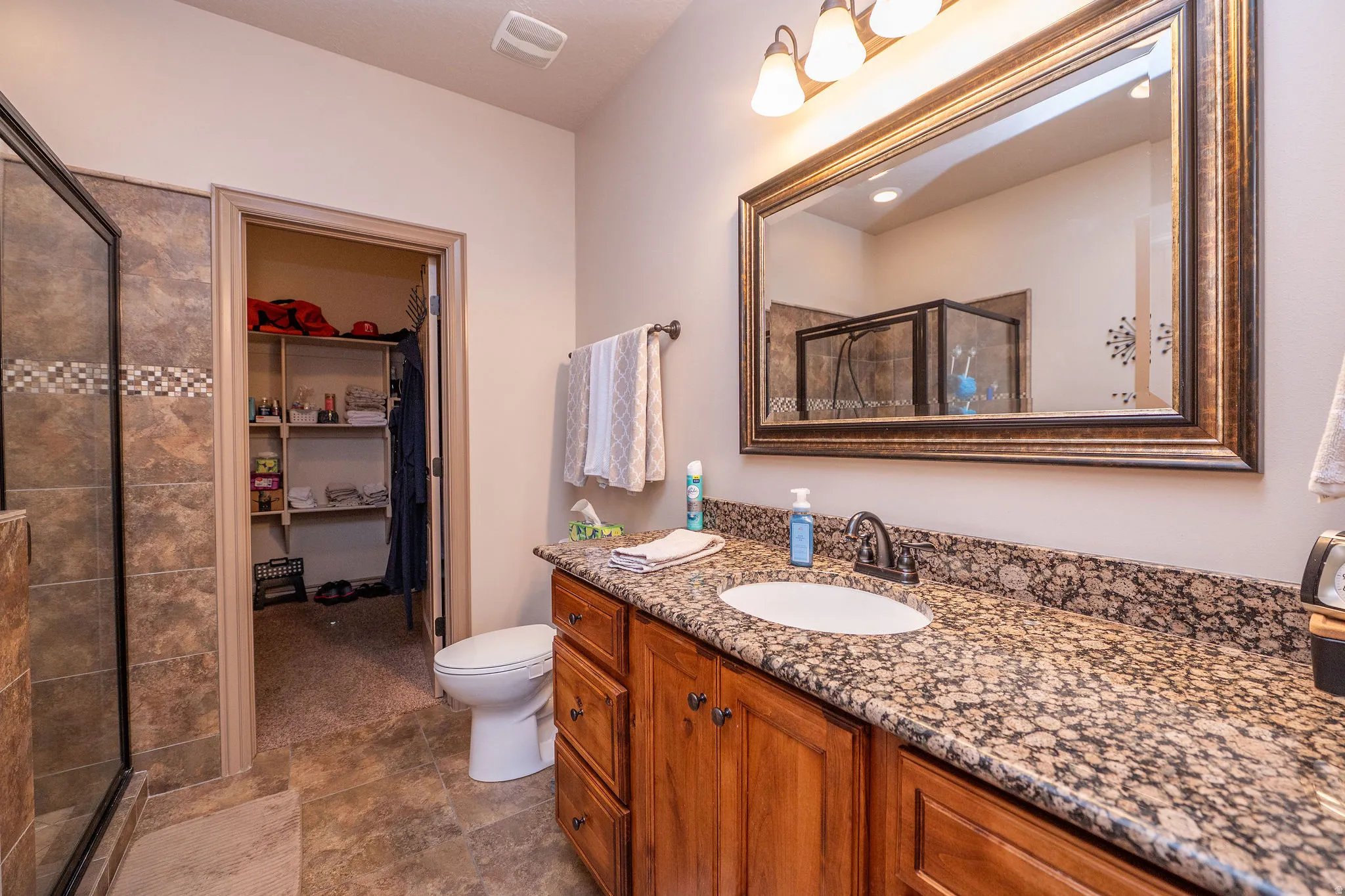 Beautifully appointed ensuite with knotty alder cabinetry, granite countertop, framed mirror, tiled walk-in shower with glass door, and direct access to the walk-in closet. Everything a primary suite should have.