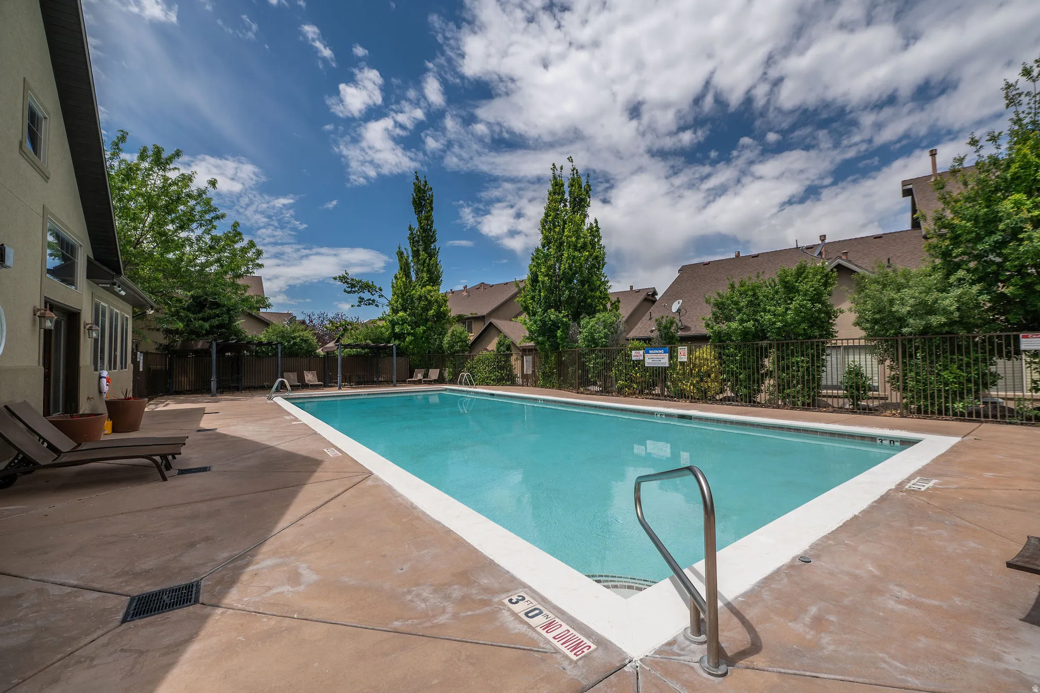 Second angle of the pool showcases the spacious concrete deck, lounge seating, lush landscaping, and the beautiful Utah sky overhead. Well-maintained and ready for the season.