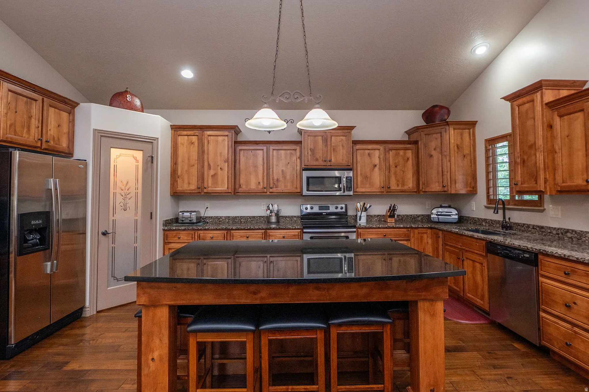 Gorgeous kitchen featuring knotty alder cabinetry, dark granite island with bar seating, stainless appliances, hardwood floors, and a charming etched glass pantry door. This kitchen means business.