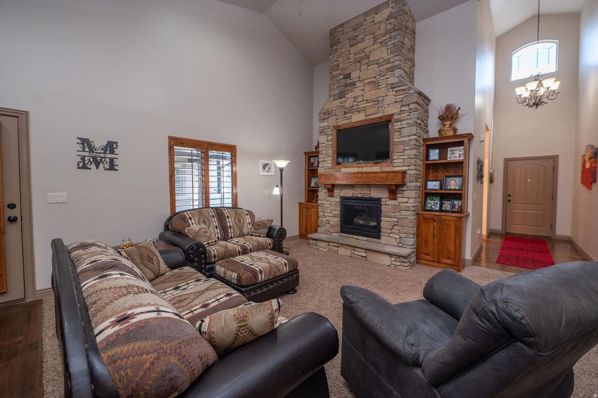 Show-stopping great room with vaulted ceilings, floor-to-ceiling stacked stone fireplace, built-in wood cabinetry, and a chandelier in the entry beyond. This room owns the whole house.